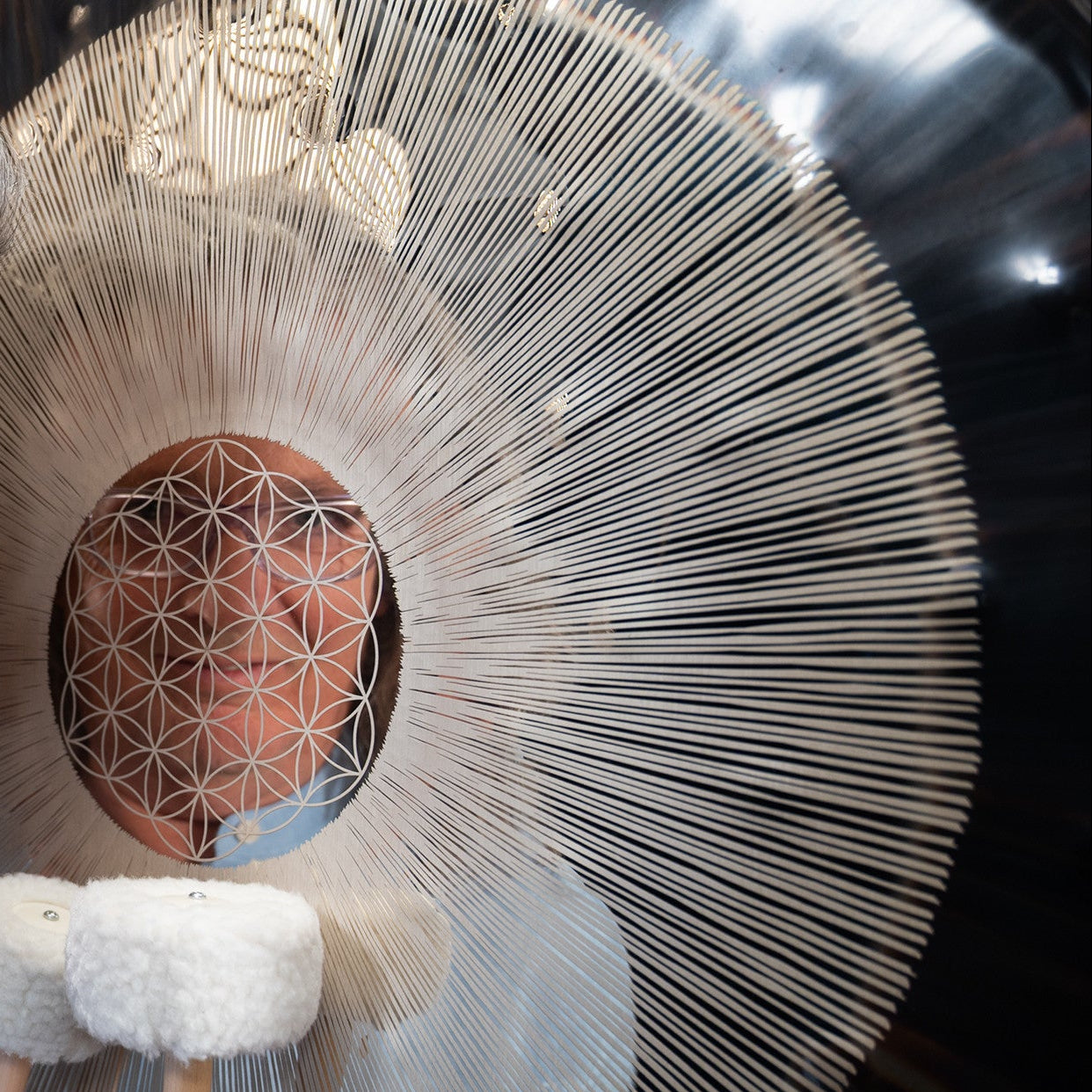 Person interacting with a large, intricate percussion gong resembling a flower of life mandala.